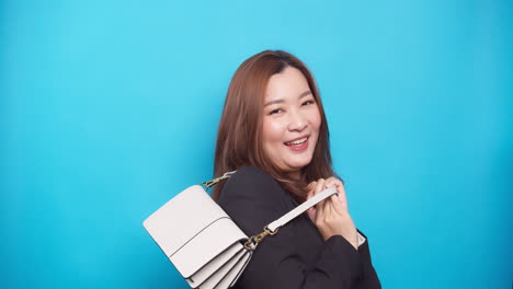 Porträt-Einer-Asiatischen-Frau,-Die-Eine-Handtasche-Hält,-Lächelnd-Und-Glücklich-Auf-Blauem-Hintergrund