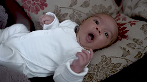 Adorable-One-Month-Old-Baby-Yawning,-Laying-On-Back-On-Sofa-Cushions