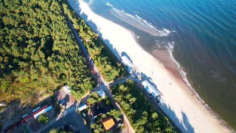 Aerial-flyover-forest-path,-sandy-beach-and-waves-of-Baltic-Sea-lighting-in-sun---Poland,Europe