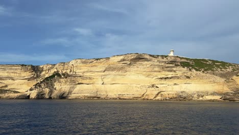 Sunlight-on-cliff-of-Capo-Pertusato-lighthouse-in-Corsica-island-as-seen-from-sailing-boat,-France