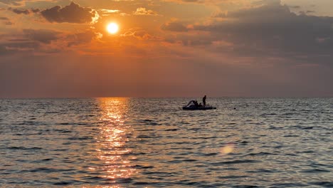 Wunderschöner-Goldener-Sonnenuntergang-Und-Silhouetten-Von-Menschen,-Die-Von-Einem-Tretboot-Ins-Meer-Springen