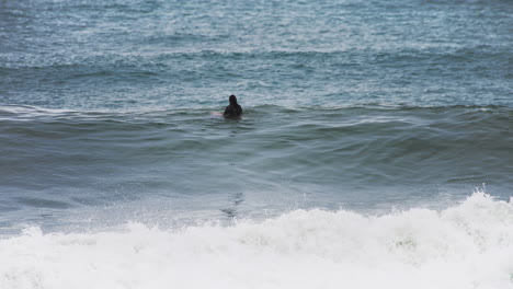 Surfer,-Der-Im-Brett-Sitzt-Und-An-Einem-Tag-Mit-Schwierigen-Wetterbedingungen-Auf-Eine-Welle-Am-Ufer-Wartet