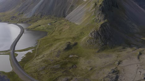 Aerial-tilt-up-shot-of-car-driving-on-road-along-coast-and-mystic-covered-Eystrahorn-Mountain-in-Iceland