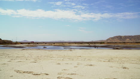 An-Einem-Sonnigen-Tag-Kann-Man-Den-Gelben-Sand-Des-Zorritos-strandes-In-Tumbes-In-Peru-Mit-Mehreren-Autos-Sehen,-Die-In-Der-Ferne-Fahren