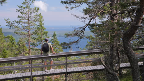 Hiking-man-walking-across-a-wooden-bridge-enjoying-views-of-Nordic-panorama