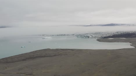 Nähernde-Luftaufnahme-Einer-Mystischen-Wolkenlandschaft,-Die-Den-Gletschersee-In-Island-Bedeckt