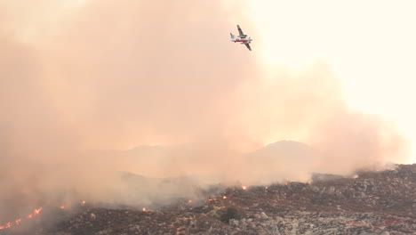 Firefighters-plane-flying-over-grey-smoke,-coming-up-from-a-wildfire-burning