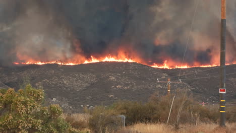 Massive-flames-and-smoke-clouds-cover-hill-ridge-in-Hemet,-California