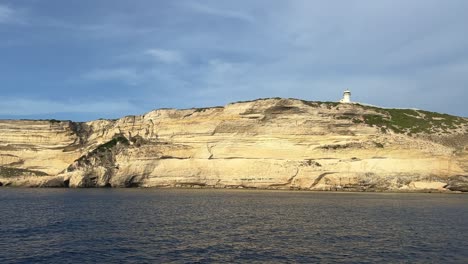 Sunlight-on-cliff-of-Capo-Pertusato-lighthouse-in-Corsica-island-as-seen-from-sailing-boat,-France-1