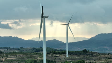 Inoperative-wind-turbines-and-mountainous-landscape-of-Coll-de-Moro-in-background-with-cloudy-stormy-sky,-Catalonia-in-Spain
