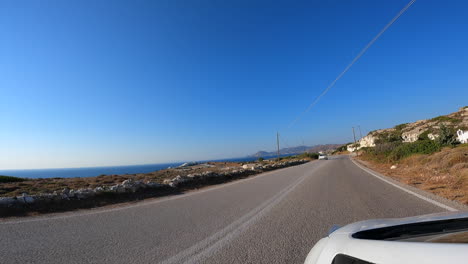 Blickwinkel:-Ein-Weißes-Auto-Fährt-Auf-Einer-Zweispurigen-Griechischen-Straße,-Sommerferien,-Blick-Auf-Das-Mittelmeer