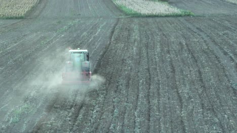Aerial-tracking-shot-of-tractor-plowing-agriculture-field-and-make-dust