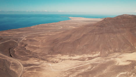 Aerial-with-sweeping-coastal-views-of-barren-landscape-with-rugged-mountains---Playa-de-Cofete,-Fuerteventura
