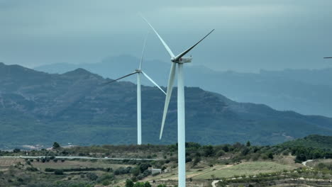 Aerial-parallax-panoramic-view-of-eolic-wind-turbines-in-rural-mountain-landscape-on-cloudy-day-at-Coll-de-Moro-in-Catalonia,-Spain
