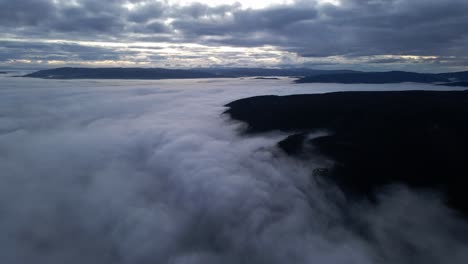 Aerial-view-on-top-of-the-clouds-of-a-mountain-with-a-forest-rising-above-the-clouds