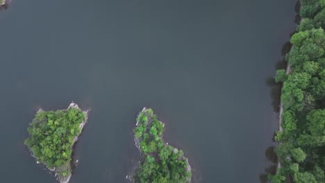 An-aerial,-top-down-view-over-calm-waters-with-tiny-islands-with-green-trees-on-a-cloudy-day