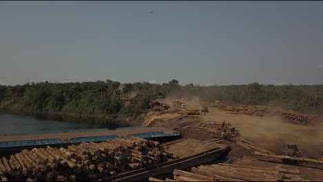 Deforestation-of-the-Amazon-rainforest:-stacking-logs-on-barges-for-transport---aerial-flyover