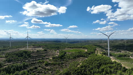 Drone-aerial-view-of-wind-turbines-and-green-landscape-with-blue-sky-in-Catalonia,-Spain