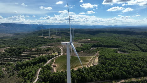 Wind-turbines-with-blades-spinning-and-surrounding-countryside-landscape,-Coll-de-Moro-wind-farm,-Catalonia-in-Spain
