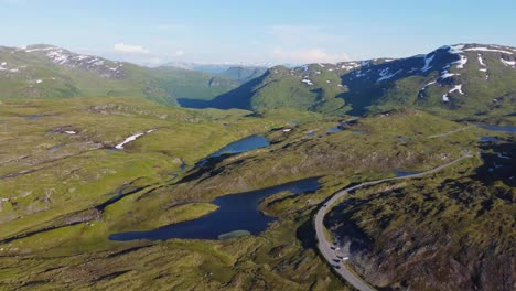 Curvy-mountain-road-with-passing-cars-on-top-of-Vikafjell-mountain-Norway---Evening-summer-sunset-aerial-view-with-Myrkdalen-valley-in-background