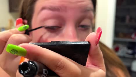 Close-up-of-Young-Woman-Putting-Mascara-on-Eyelash-While-Holding-Small-Portable-Mirror