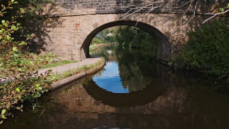 Drone-footage-of-a-canal-with-a-stone-built-bridge-set-in-Hebden-Bridge,-Yorkshire-England