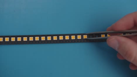 Manually-Picking-LEDs-with-Tweezers-from-a-Black-Strip-Blue-Background