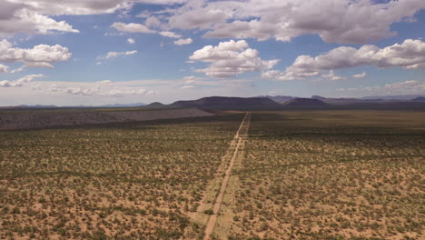 Road-leading-into-the-distance-in-vast-Southern-Arizona-landscape,-drone-backwards