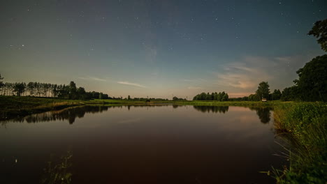 Time-lapse-of-stars-in-starry-sky-reflecting-over-lake-water-surface-at-sunrise-and-headlights-of-cars-driving-along-river-or-lake-bank