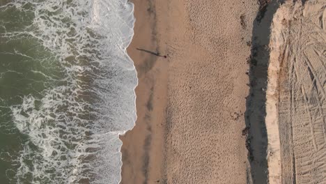 Aerial-Drone-Top-Down-Shot-of-Person-Running-along-the-beach-at-Low-Tide-with-waves-Crashing-on-the-Shoreline