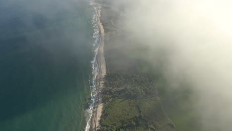 Beautiful-Cinematic-Aerial-Drone-Shot-of-a-Tropical-Shoreline-being-Revealed-Through-Clouds