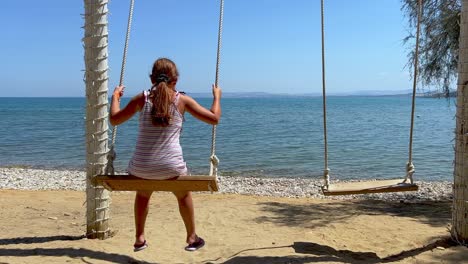 Redhead-little-girl-on-summer-holiday-enjoy-swinging-on-rope-swing-looking-at-calm-sea