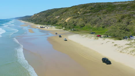 Aerial-Drone-Of-Cars-Driving-Along-Sandy-Beach-Shore-Beside-Ocean-Waves,-4K