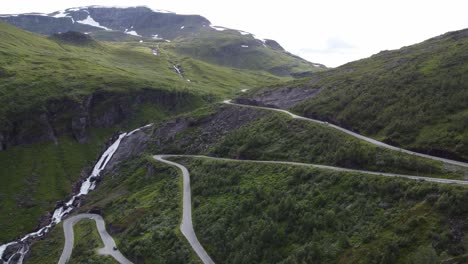 Halsabakkane-winding-roads-at-Vikafjellet-mountain-crossing-close-to-Myrkdalen-in-western-Norway---Beautiful-aerial-sideview-of-lush-mountain-meadow-with-road-in-hillside