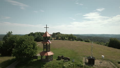 Panorama-Landschaftsaufnahme-Eines-Hügels-Mit-Kleinem-Turm-Auf-Der-Spitze-Und-Wald-Mit-Bäumen-Um-Sie-Herum,-Schöner-Blauer-Himmel-Und-Hügel-Im-Hintergrund-In-Slowenien,-Luftdrohnenaufnahme