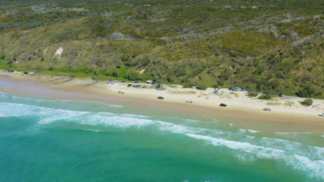 Blue-Ocean-Waves-Beside-4WD-Cars-Driving-Along-Sandy-Beach-Shore,-4K-Aerial-Drone