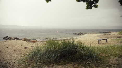 Empty-beach-with-dune-grass-and-wooden-bank-in-the-front-on-a-overcast-day-at-fjord