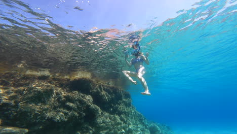 A-young-girl-swims-on-the-surface,-underwater-view-from-below,-scuba-diving-on-vacation