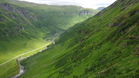 Deep-lush-green-valley-of-Vikafjell-and-Myrkdalen-with-sun-patches-on-road-in-bottom---Beautiful-aerial-moving-downwards-along-steep-mountainside---Norway
