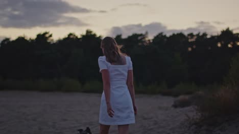 Tilt-down-of-attractive-young-woman-walking-through-sand-dunes-at-dusk-with-her-dog
