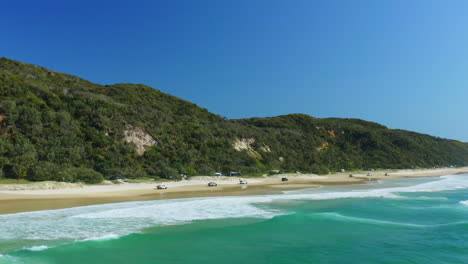 4WD-Cars-Driving-Along-Sandy-Beach-Shore-Beside-Blue-Ocean-Waves-In-Australia,-4K-Aerial-Drone