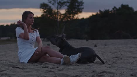 Young-woman-playing-fetch-with-a-American-Staffordshire-Terrier-in-sand-dunes-at-dusk