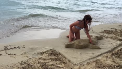 Little-girl-on-vacation-plays-on-beach-building-sand-dolphin-on-seashore