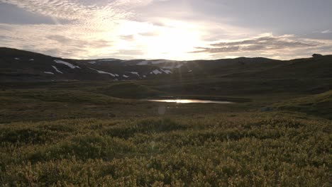 Wunderschöner-Sonnenuntergangszeitraffer-Mit-Goldenem-Licht-Und-Vorbeiziehenden-Wolken-Am-Berg-Vikafjell-In-Westnorwegen---Sonnenreflexionen-In-Einem-Kleinen-Teich-Und-Lichtstrahlen,-Die-Auf-Linse-Und-Blaubeerheide-Im-Vordergrund-Treffen
