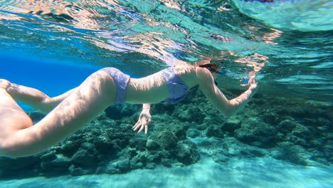 A-young-girl-swims-and-films-with-her-phone-the-wildlife-near-a-coral,-underwater