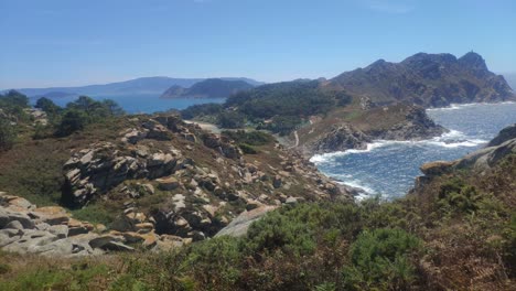 Mountainous-island-with-cliffs-and-beaches-with-heat-mist,-sunny-day,-panoramic-shot-turning-slow-to-the-right,-Cíes-Islands,-Pontevedra,-Galicia,-Spain