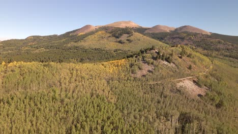 Flying-along-an-aspen-covered-ridge-with-a-dirt-road-towards-treeless-summits