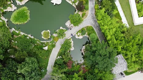 Aerial-bird's-eye-view-with-counterclockwise-helix-of-a-pond-in-a-beautiful-Chinese-garden-on-a-sunny-afternoon-at-Huancui-lou-park,-Weihai-city,-China