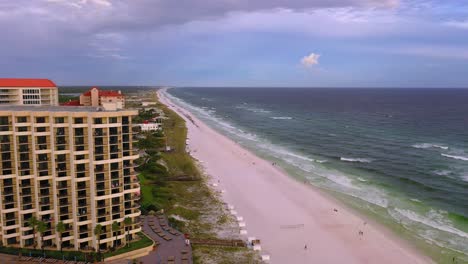 Drone-view-flying-down-the-white-sand-beach-of-San-Destin-FL-past-some-condos-during-golden-hour-with-some-dark-clouds-in-the-sky
