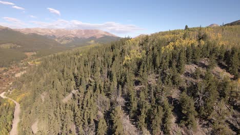Aerial-view-rotating-over-a-road-and-aspen-covered-ridge-to-reveal-distance-mountains-above-treeline
